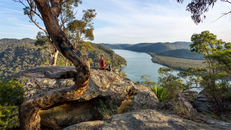 Female sitting on a large rock relaxing in afternoon dappled light the Australian bushland with views over the river.